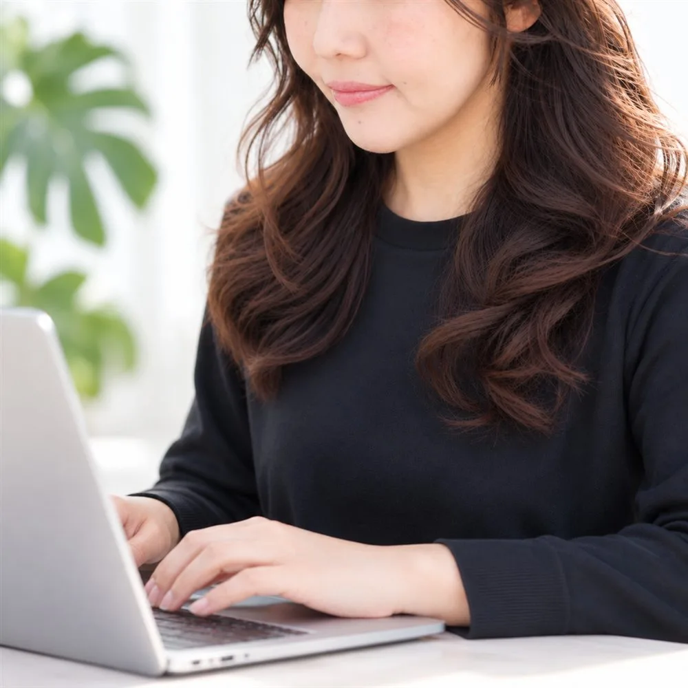 ノートパソコンに向かって作業する亜紀